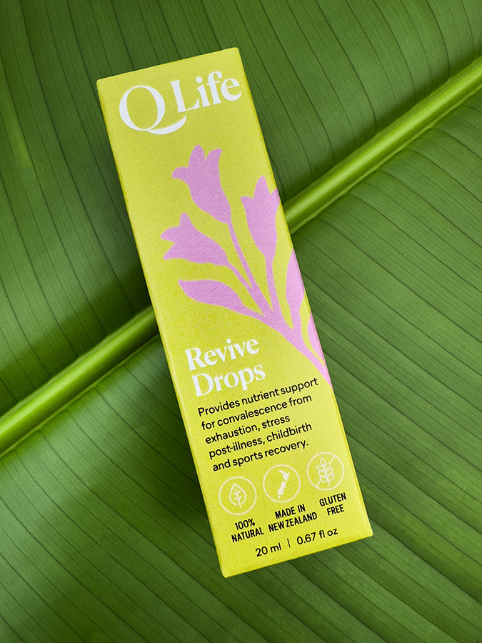 Q Life Revive Drops box on a green leaf, highlighting the product's natural ingredients.